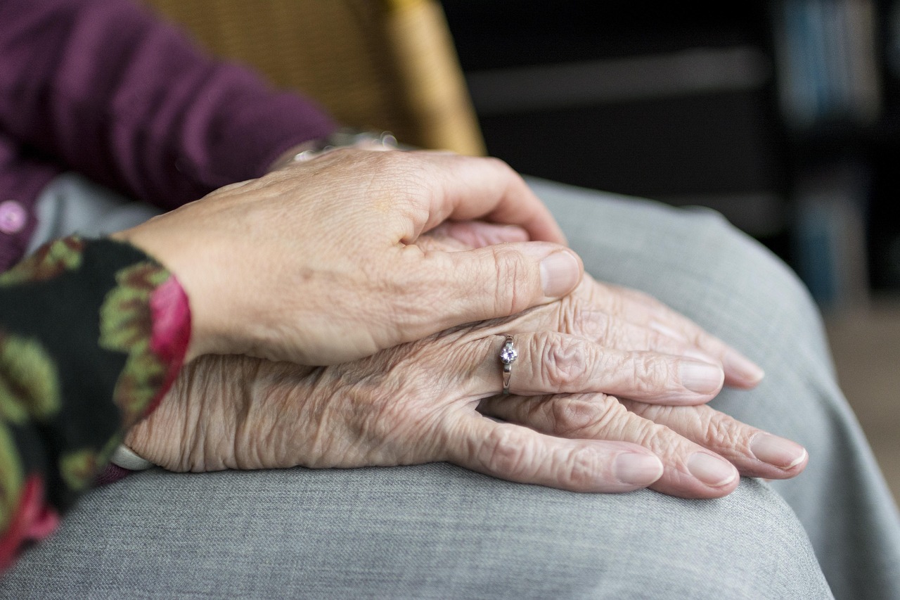 Nahansicht von zwei übereinandergelegten Händen. Die Hand einer Frau mittleren Alters liegt auf der Hand einer älteren Frau.